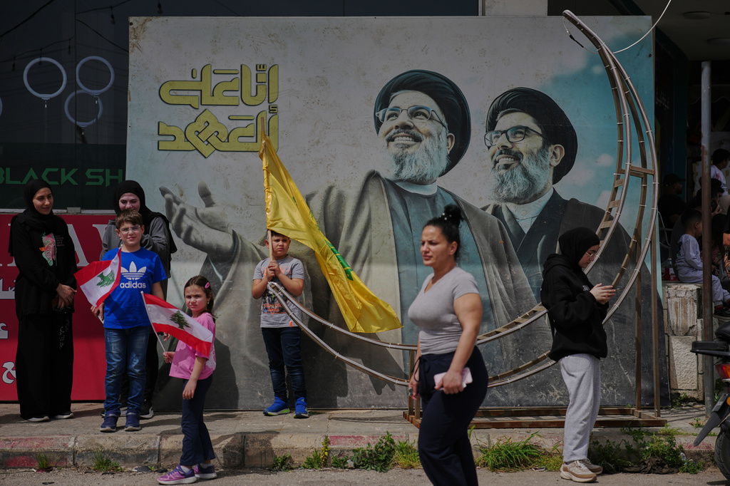 People stand next to a mural with the images of late Hezbollah leaders Hassan Nasrallah, left, and Hashem Safieddine as displaced residents return to their villages following a ceasefire between Israel and Hezbollah, in Zefta, southern Lebanon, Friday, April 17, 2026. (AP Photo/Hassan Ammar)