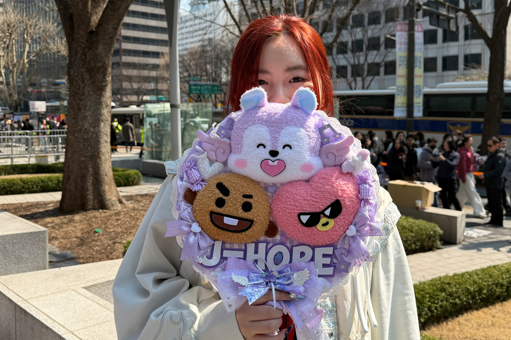 Han Yunyi, BTS fan originally from Jiangsu province in China, poses for a photo holding BTS fan merchandise ahead of BTS's comeback concert near Gwanghwamun Square in Seoul, South Korea, Saturday, March 21, 2026. (AP Photo/ Juwon Park)
