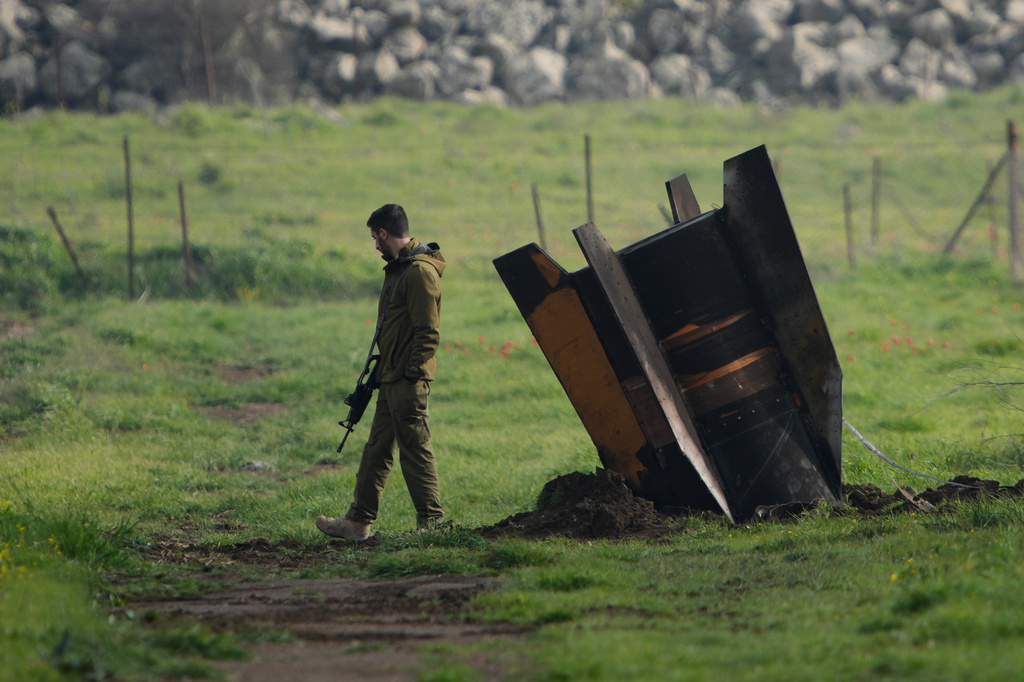 FILE - An Israeli soldier stands next to a fragment of a missile fired from Iran and intercepted by Israeli air defense system embedded in an open field in the Israeli-controlled Golan Heights, March 19, 2026. (AP Photo/Ohad Zwigenberg, File)