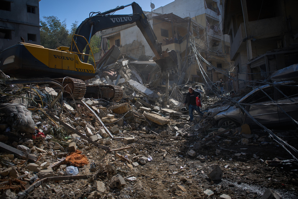 An excavator works removing the rubble as people walk at the site of Sunday's Israeli strike on a building in Beirut's Jnah neighborhood, Lebanon, Monday, April 6, 2026. (AP Photo/Emilio Morenatti)