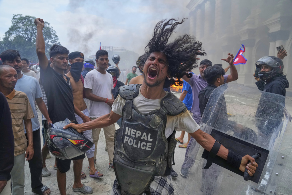 A protester wearing flak jacket and carrying a shield snatched from a policeman shouts slogans at the Singha Durbar, the seat of Nepal's government's various ministries and offices during a protest against social media ban and corruption in Kathmandu, Nepal, Tuesday, Sept. 9, 2025. (AP Photo/Niranjan Shrestha)