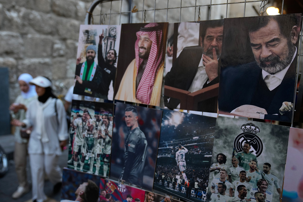 Women pass portraits showing the late Iraqi President Saddam Hussein, right, and the Saudi Crown Prince Mohammed bin Salman in the old city of Damascus, Syria, Thursday, Oct. 2, 2025. (AP Photo/Hussein Malla)