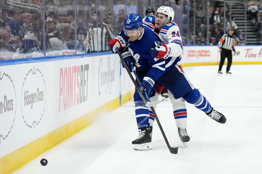 Toronto Maple Leafs defenseman Jake McCabe (22) gets checked by New York Rangers forward Tye Kartye (24) during the third period of an NHL hockey game, in Toronto, Wednesday, March 25, 2026. (Nathan Denette/The Canadian Press via AP)