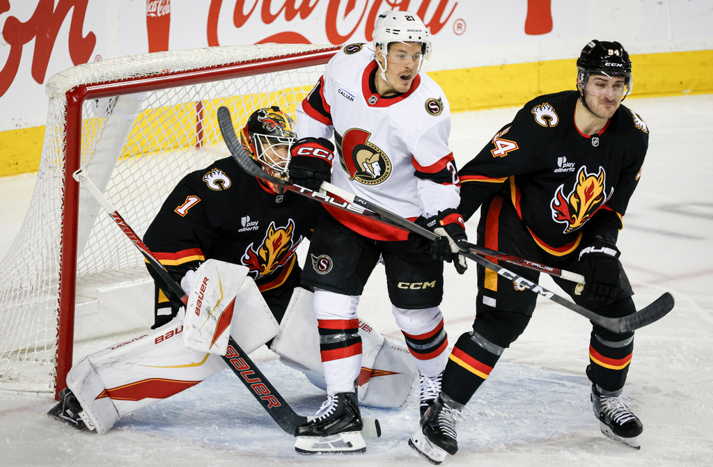 Ottawa Senators' Nick Cousins, centre, is checked by Calgary Flames' Brayden Pachal, right, in front of goalie Devin Cooley during the second period of an NHL hockey game in Calgary on Thursday, March 5, 2026. (Jeff McIntosh/The Canadian Press via AP)