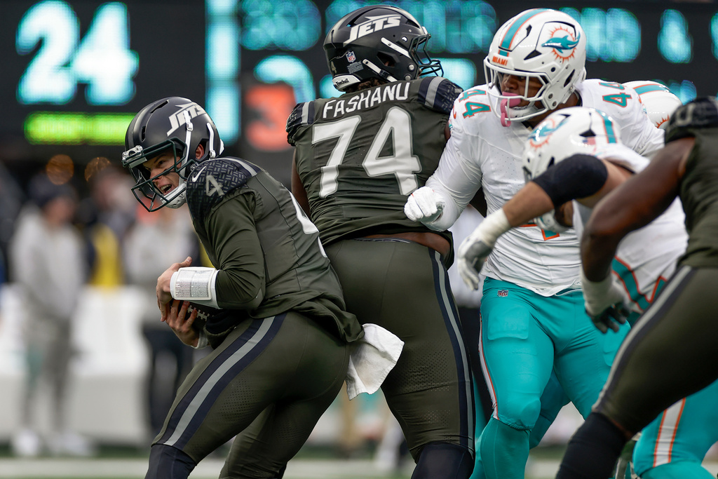 New York Jets quarterback Brady Cook (4) tucks the ball under pressure from the Miami Dolphins during the third quarter of an NFL football game, Sunday, Dec. 7, 2025, in East Rutherford, N.J. (AP Photo/Adam Hunger)