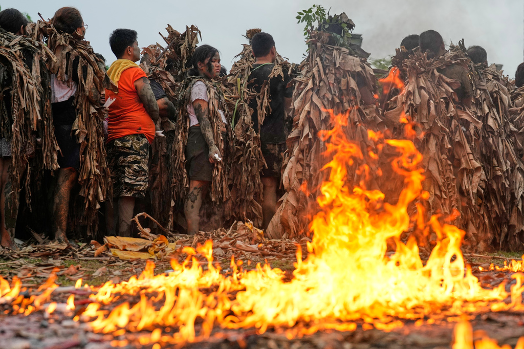 Catholic devotees covered in mud and dried banana leaves stands beside burning candles during the mud people festival on the feast day of Saint John the Baptist at Bibiclat, Nueva Ecija province, northern Philippines on Wednesday, June 24, 2026. (AP Photo/Aaron Favila)