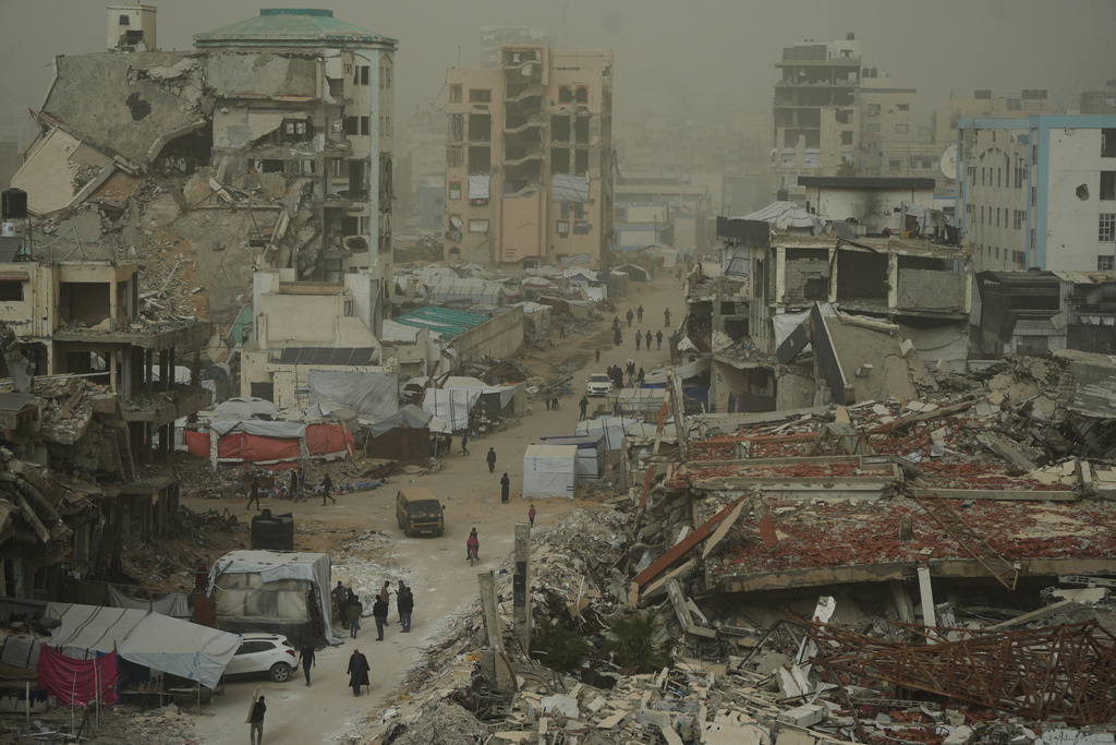 FILE - Palestinians walk along a street surrounded by buildings destroyed in Israeli air and ground operations during a dust storm in Gaza City, Saturday, Feb. 14, 2026. (AP Photo/Jehad Alshrafi)
