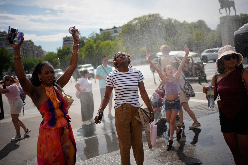 Tourists enjoy cooling off at a public water fountain In Paris, Friday, June 26, 2026. (AP Photo/Christophe Ena )