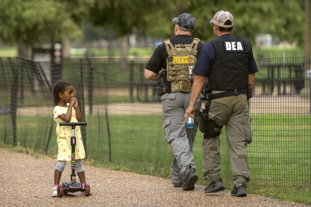 A child watches as officers with the Drug Enforcement Administration patrol along the National Mall Wednesday, Aug. 13, 2025, in Washington. (AP Photo/Mark Schiefelbein)