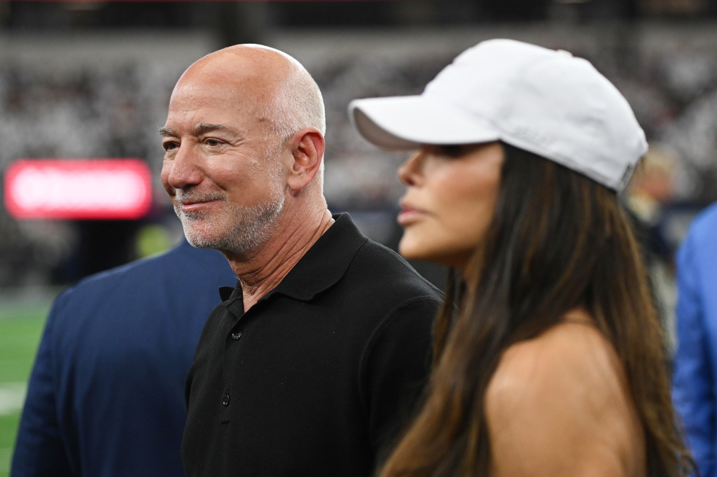 Jeff Bezos, left, stands on the field with his wife Lauren Sanchez Bezos prior to an NFL football game between the Dallas Cowboys and the Washington Commanders in Arlington, Texas, Sunday, Sept. 20, 2026. (AP Photo/Jessica Tobias)