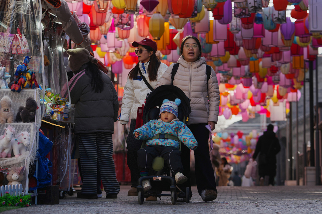 FILE - Women push a toddler on a stroller as they tour the Qianmen shopping street with lantern decorations in Beijing, China on Jan. 12, 2026. (AP Photo/Andy Wong, File)