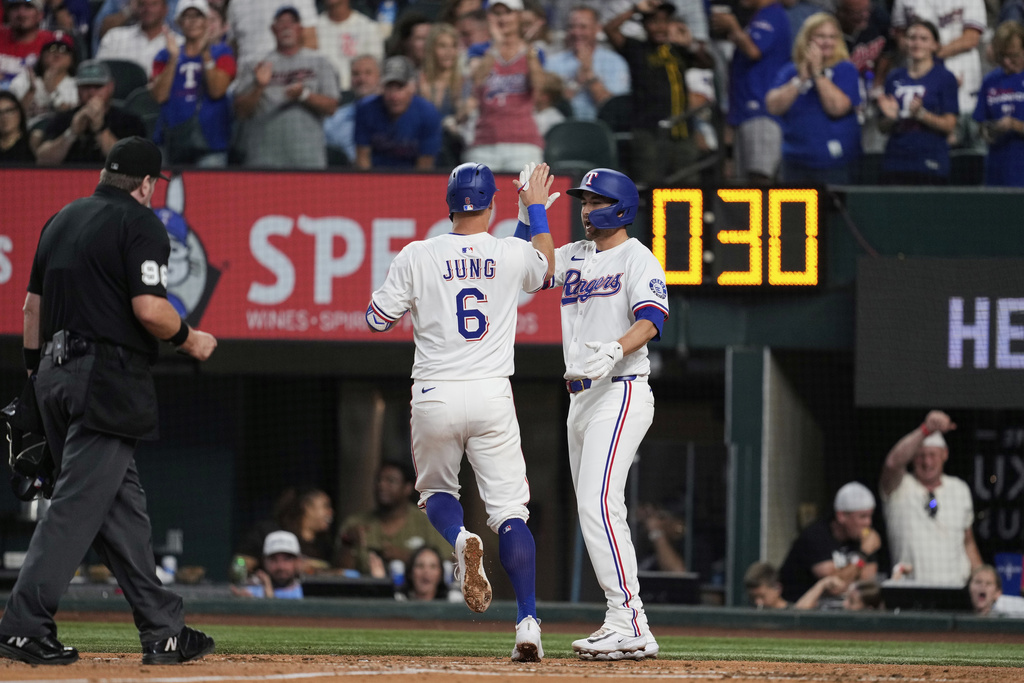 Texas Rangers' Josh Jung (6) and Kyle Higashioka, right, celebrate Jung's two run home run that scored Higashioka as umpire Chris Conron, left, looks on in the third inning of a baseball game against the Cleveland Guardians Saturday, Aug. 23, 2025, in Arlington, Texas. (AP Photo/Tony Gutierrez)