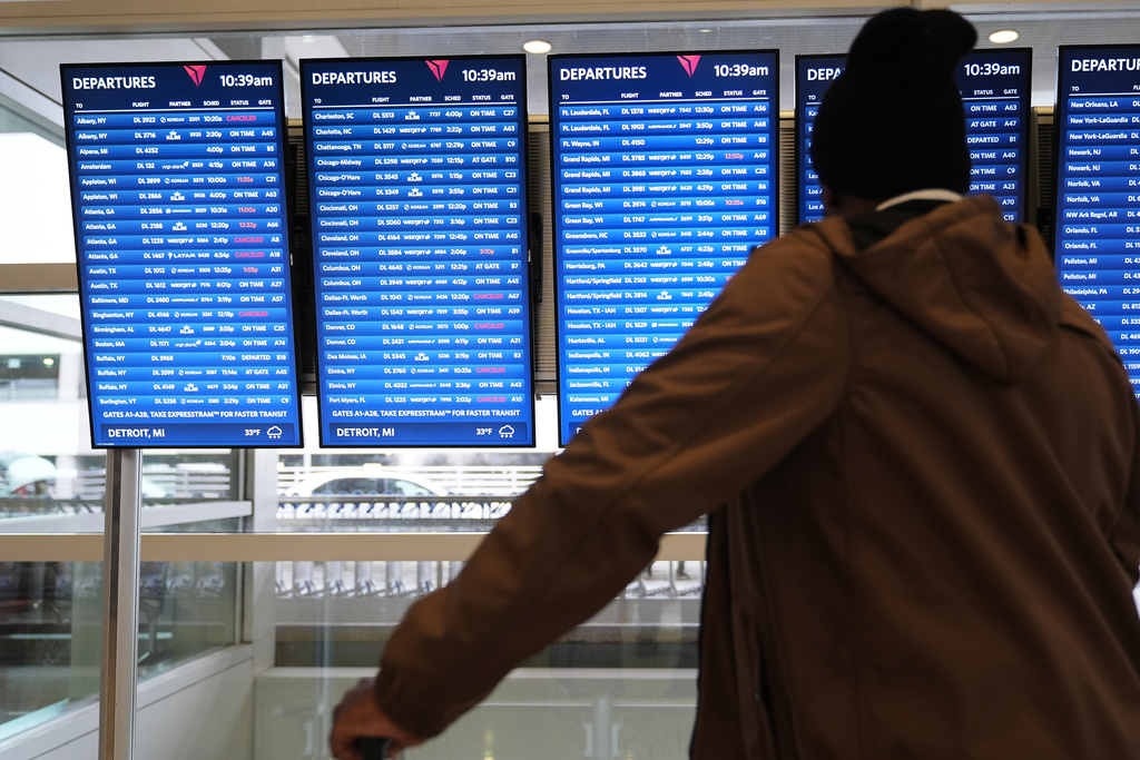 Travelers wait at a video board at the Detroit Metropolitan Airport, Sunday, Nov. 9, 2025, in Detroit. (AP Photo/Ryan Sun)