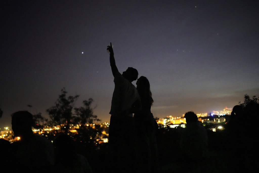 A young couple stands on a wall looking at the sky at a viewpoint overlooking Lisbon during a nationwide power outage, Monday, April 28, 2025. (AP Photo/Armando Franca)