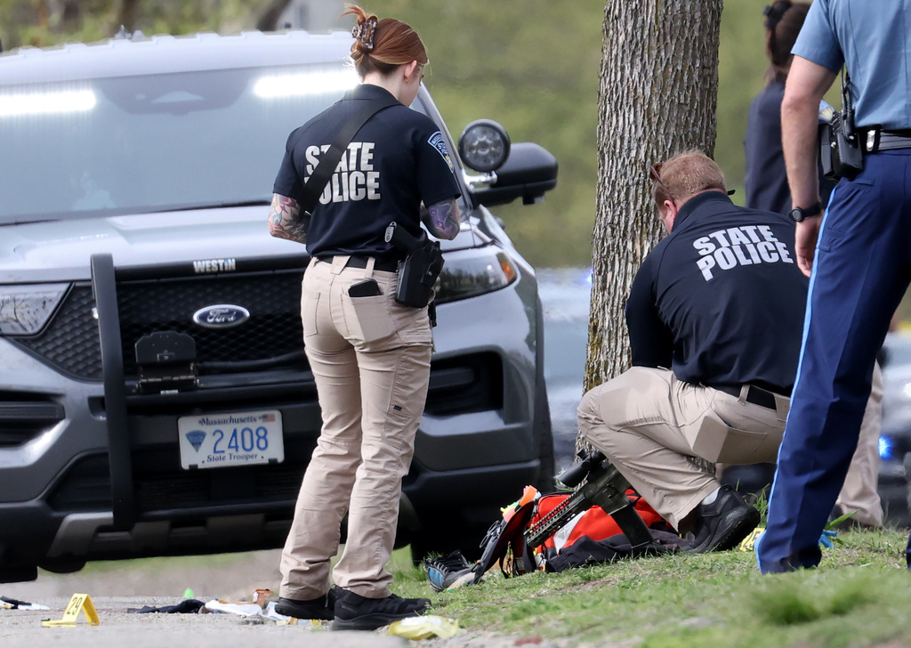 A member of the State Police bends to pick up a gun on Memorial Drive in Cambridge, Mass., Monday, May 11, 2026. (Jessica Rinaldi/The Boston Globe via AP)