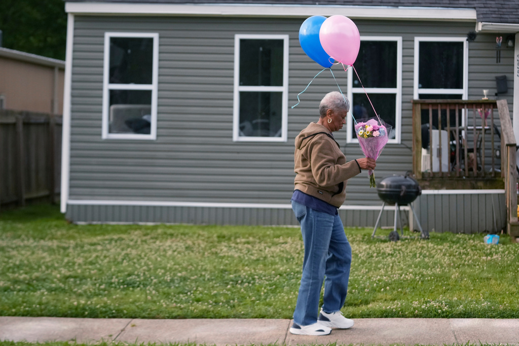 A woman walks to leave flowers and balloons on the front lawn of the home where children were killed during a mass shooting the day before in Shreveport, La., Monday, April 20, 2026. (AP Photo/Gerald Herbert)