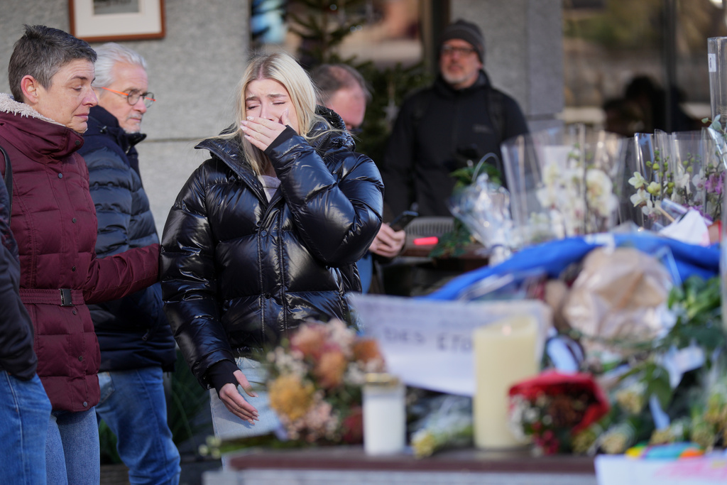 People bring flowers near the sealed off Le Constellation bar, where a devastating fire left dead and injured during the New Year's celebrations in Crans-Montana, Swiss Alps, Switzerland, Friday, Jan. 2, 2026. (AP Photo/ Antonio Calanni)