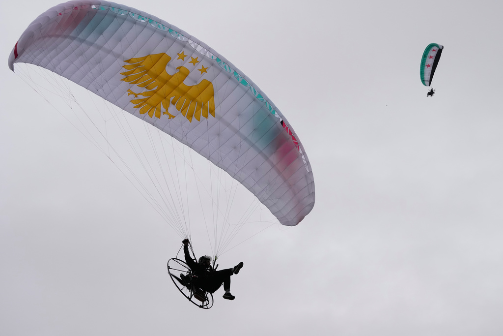 Powered paragliders fly over a gathering during celebrations marking the first anniversary of the ousting of former President Bashar Assad, with Mount Qasioun seen in the background, in Damascus, Syria, Monday, Dec. 8, 2025. (AP Photo/Hussein Malla)