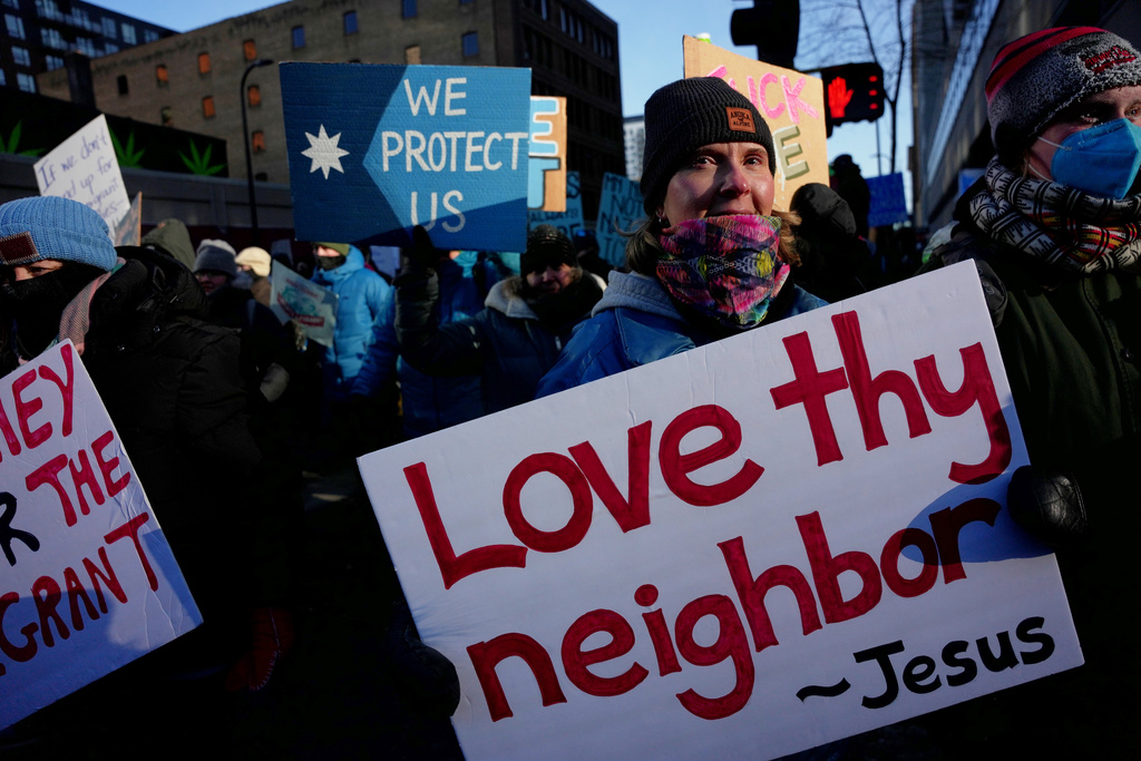 A protester holds a sign reading "Love thy neighbor - Jesus" during a rally against federal immigration enforcement on Friday, Jan. 23, 2026, in Minneapolis. (AP Photo/Angelina Katsanis)