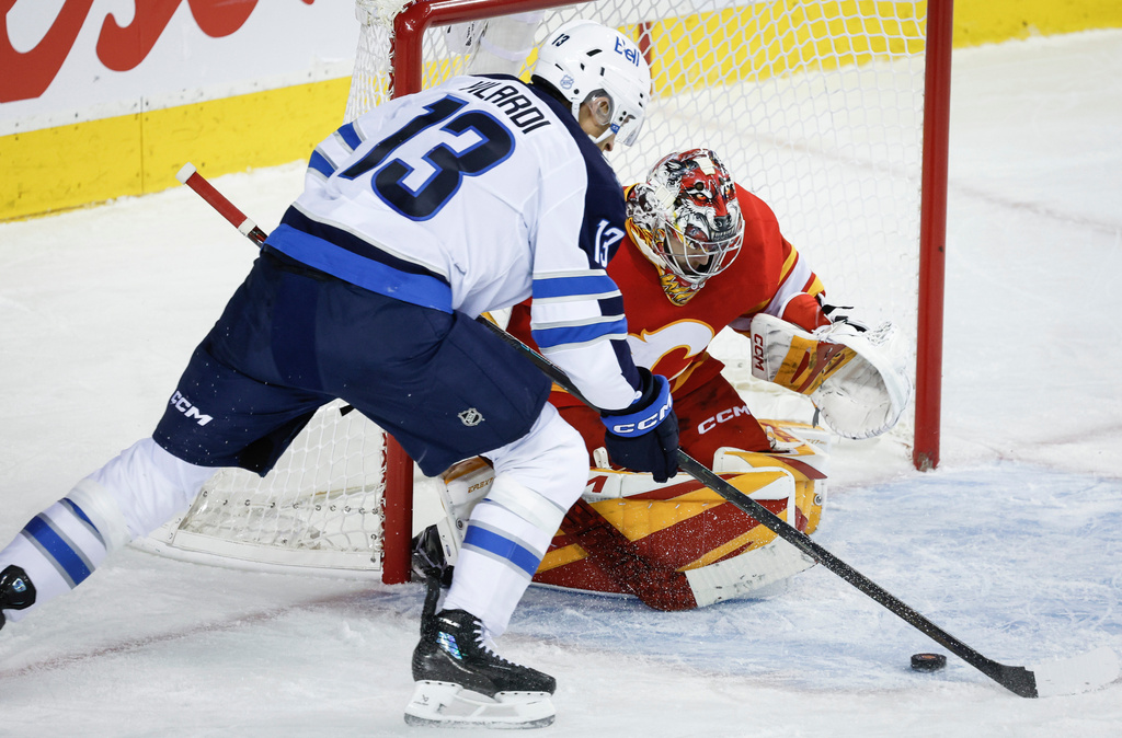 Winnipeg Jets' Gabriel Vilardi, left, tries to get the puck past Calgary Flames goalie Dustin Wolf, right, during second-period NHL hockey game action in Calgary, Alberta, Monday, Oct. 20, 2025. (Jeff McIntosh/The Canadian Press via AP)