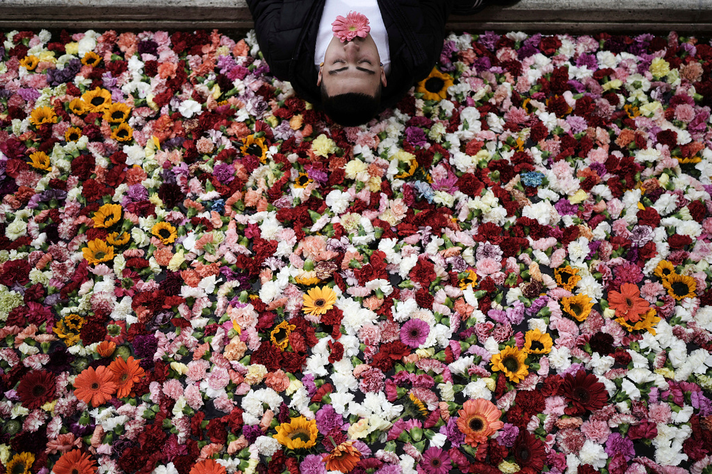 A pedestrian poses for a photo on the edge of an installation, a canal filled with flowers, during the opening of the city's first art biennial in downtown Bogota, Colombia, Saturday, Sept. 20, 2025. (AP Photo/Ivan Valencia)