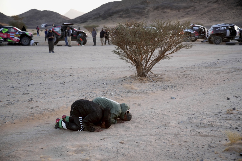 Toyota driver Yazeed Al Rajhi, left, and Ford driver Nasser Al-Attiyah pray at the bivouac area after stage two of the Dakar Rally with start in Bisha and finish in Bisha, Saudi Arabia, Sunday, Jan. 5, 2025. (AP Photo/Christophe Ena)