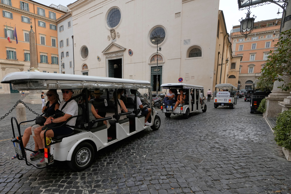 A flotilla of golf carts carrying tourists travels past the Basilica of Santa Maria sopra Minerva in Rome, Thursday, Aug. 27, 2026, as city officials move to regulate the rapidly growing industry amid complaints about congestion, illegal parking, and overtourism. (AP Photo/Gregorio Borgia)
