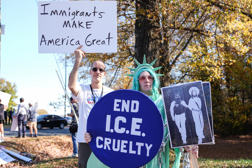 Protesters hold signs during the arrival of federal law enforcement, Wednesday, Nov. 19, 2025, in Charlotte, N.C. (AP Photo/Matt Kelley)