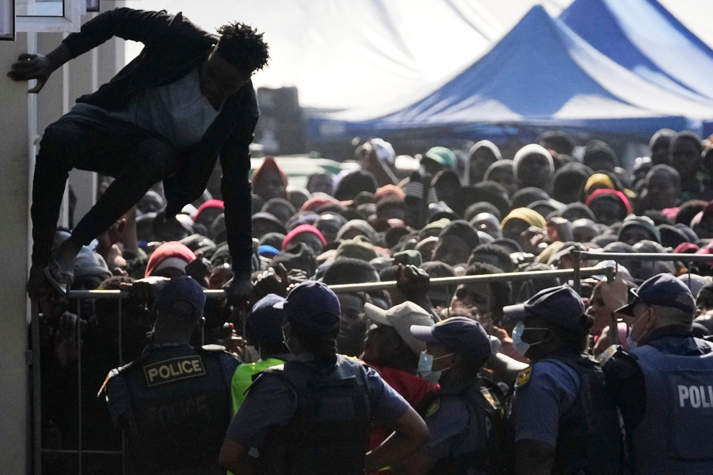 A Malawian migrant jumps over a barricade as the police officer manage the queue for their deportation at a temporary centre, in Durban, South Africa, Thursday, June 18, 2026. (AP Photo/Themba Hadebe)