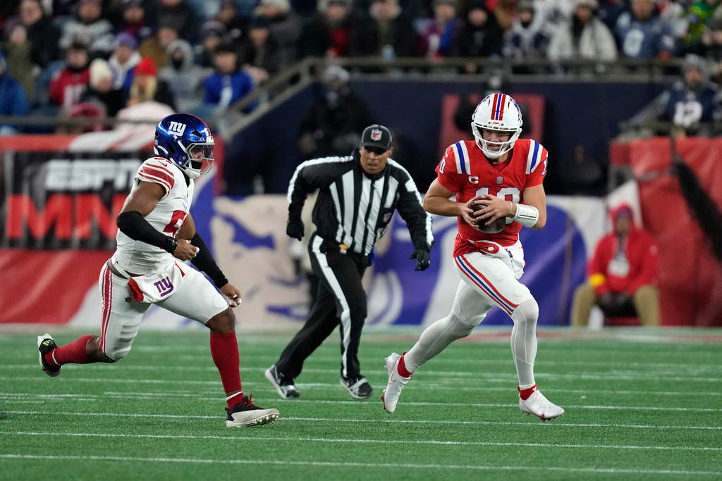 New England Patriots quarterback Drake Maye, right, runs for a first down against New York Giants linebacker Abdul Carter, left, during the second half of an NFL football game Monday, Dec. 1, 2025, in Foxborough, Mass. (AP Photo/Charles Krupa)