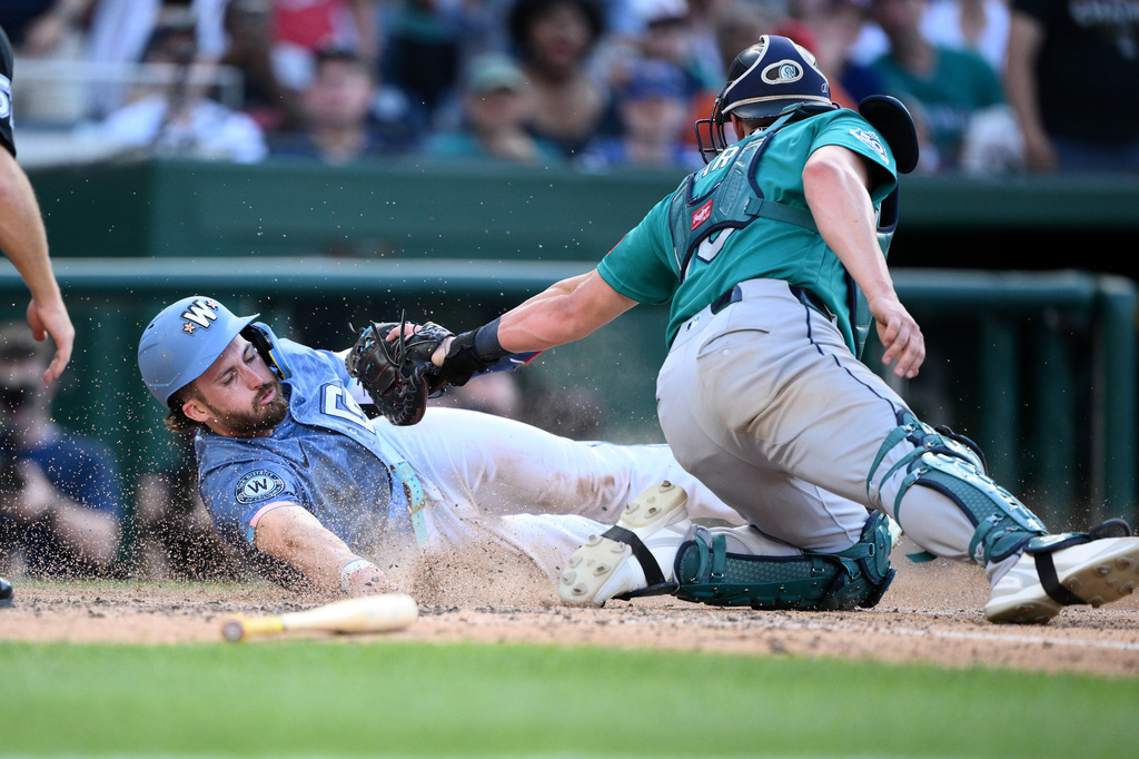 Washington Nationals' Dylan Crews, left, is safe at home plate against Seattle Mariners catcher Mitch Garver, right, during the seventh inning of a baseball game, Saturday, June 13, 2026, in Washington. (AP Photo/Nick Wass)