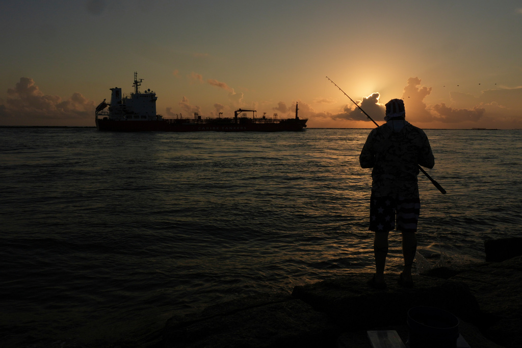 FILE - An oil tanker passes at sunrise while a man fishes in Port Aransas, Texas, Aug. 9, 2025. (AP Photo/Eric Gay, File)