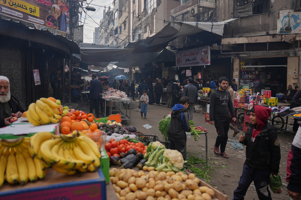 Palestinians walk along street market where fruits and vegetables are displayed for sale in Gaza City, Friday, Dec. 19, 2025. (AP Photo/Abdel Kareem Hana)