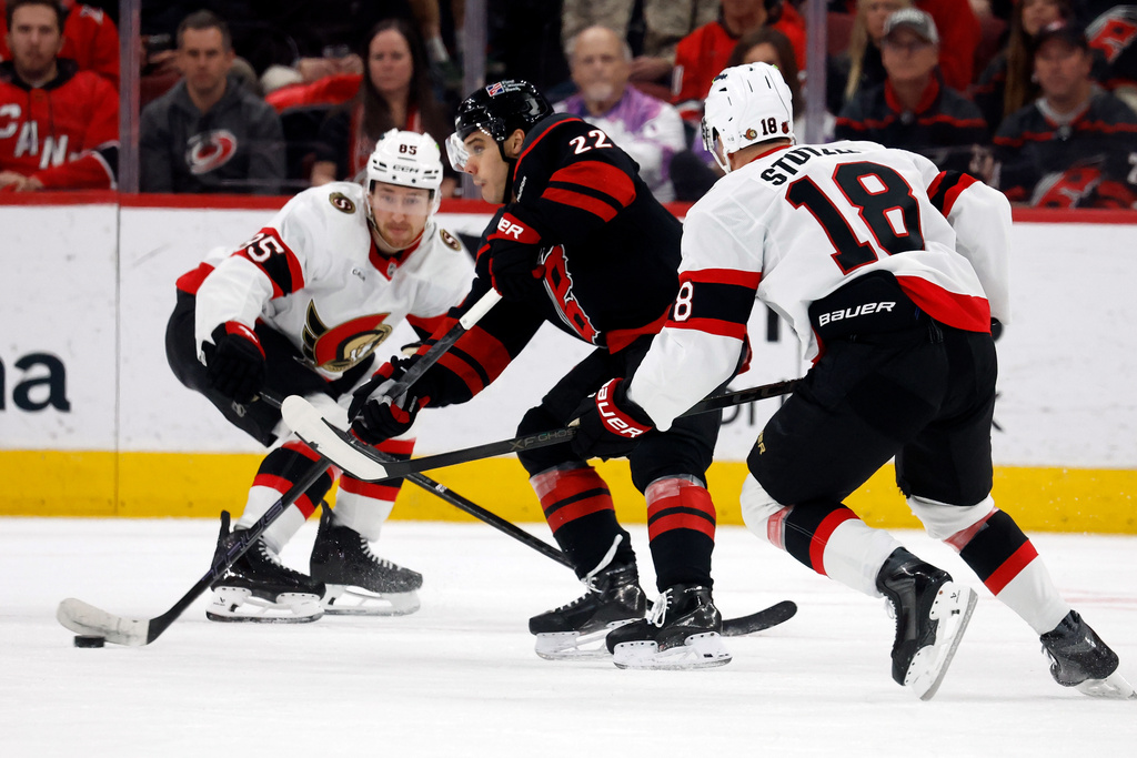 Carolina Hurricanes' Logan Stankoven (22) carries the puck between Ottawa Senators' Jake Sanderson (85) and Tim Stützle (18) during the first period of an NHL hockey game in Raleigh, N.C., Tuesday, Feb. 3, 2026. (AP Photo/Karl DeBlaker)