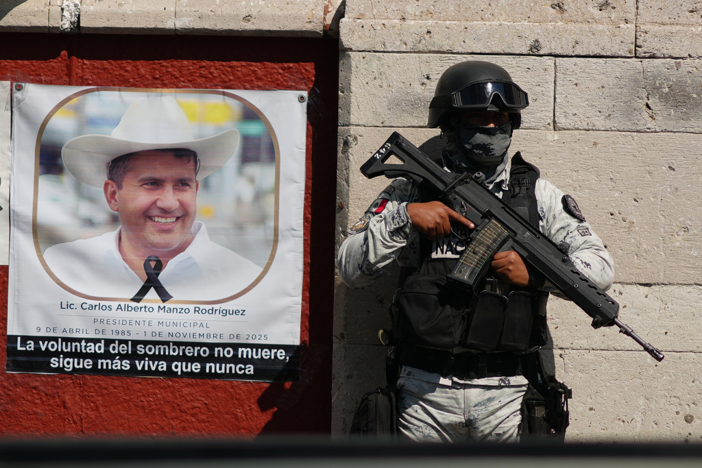 A National Guards stands guard next to a portrait of slain Mayor Carlos Manzo Rodriguez in Uruapan, Mexico, as Michoacan state prosecutors detain suspects in the investigation into his killing, Friday, Nov. 21, 2025. (AP Photo/Eduardo Verdugo)