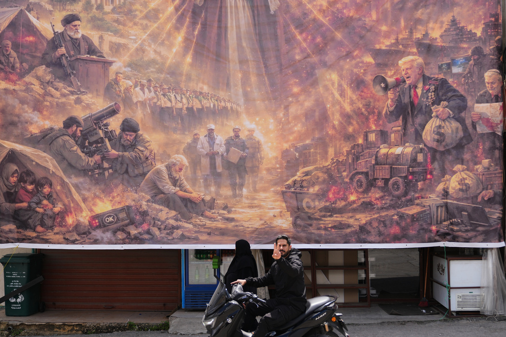 A man on a scooter flashes a victory sign as he drives past a giant portrait depicting the war in the Middle East triggered by the U.S.-Israel strikes on Iran on Feb. 28, in the southern village of Kfar Sir, Lebanon, on Tuesday, April 21, 2026. (AP Photo/Hassan Ammar)