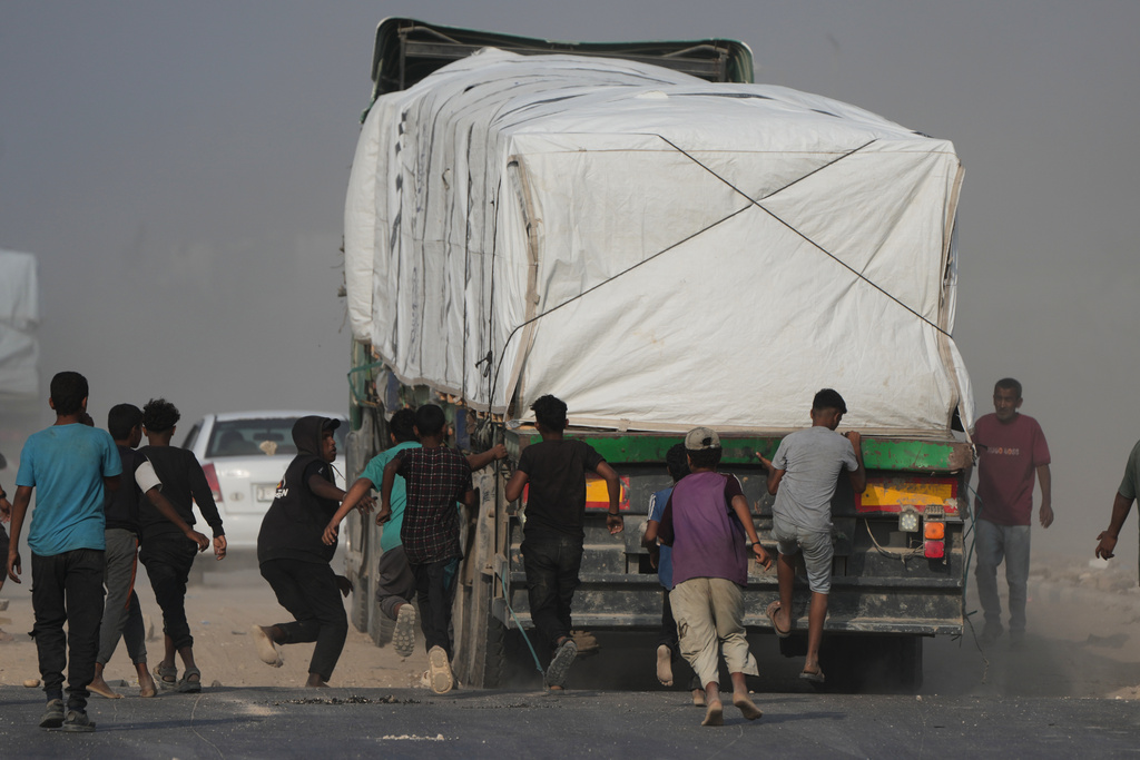 Palestinians rush toward trucks carrying aid as they drive through Deir al-Balah in central Gaza, Sunday, Nov. 9, 2025. (AP Photo/Jehad Alshrafi)