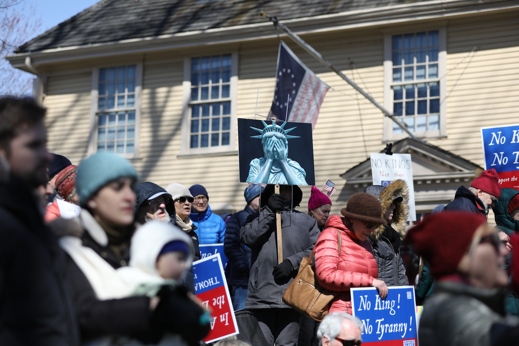 "No Kings" demonstrators hold a rally in Lexington, Mass., on Saturday, March 28, 2026, across the street from the Lexington Battle Green, where the first battle of the American Revolution took place. The old yellow building is Buckman Tavern, where revolutionaries gathered and waited for the British ahead of the battle. (Lauren Feeney/Lexington Observer via AP)