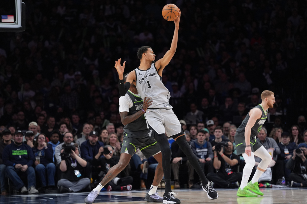 San Antonio Spurs forward Victor Wembanyama (1) grabs a pass as Minnesota Timberwolves center Naz Reid, left, defends during the second half of an NBA basketball game, Sunday, Jan. 11, 2026, in Minneapolis. (AP Photo/Abbie Parr)
