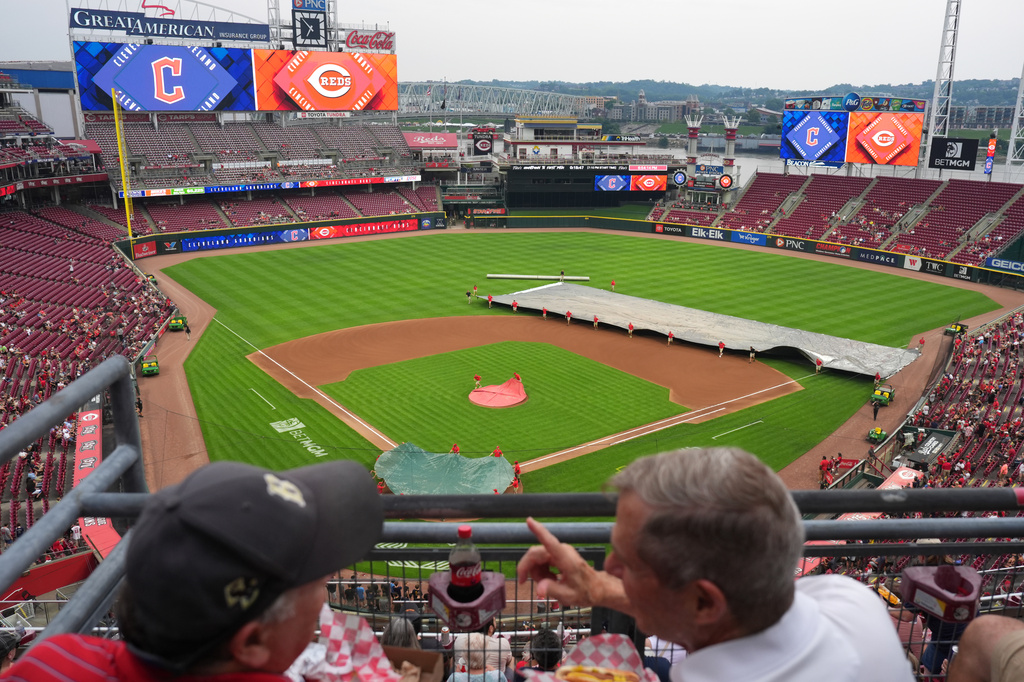 Fans talk as the Cincinnati Reds grounds crew covers the field during a rain delay before a baseball game against the Cleveland Guardians, Monday, July 27, 2026, in Cincinnati. (AP Photo/Kareem Elgazzar)