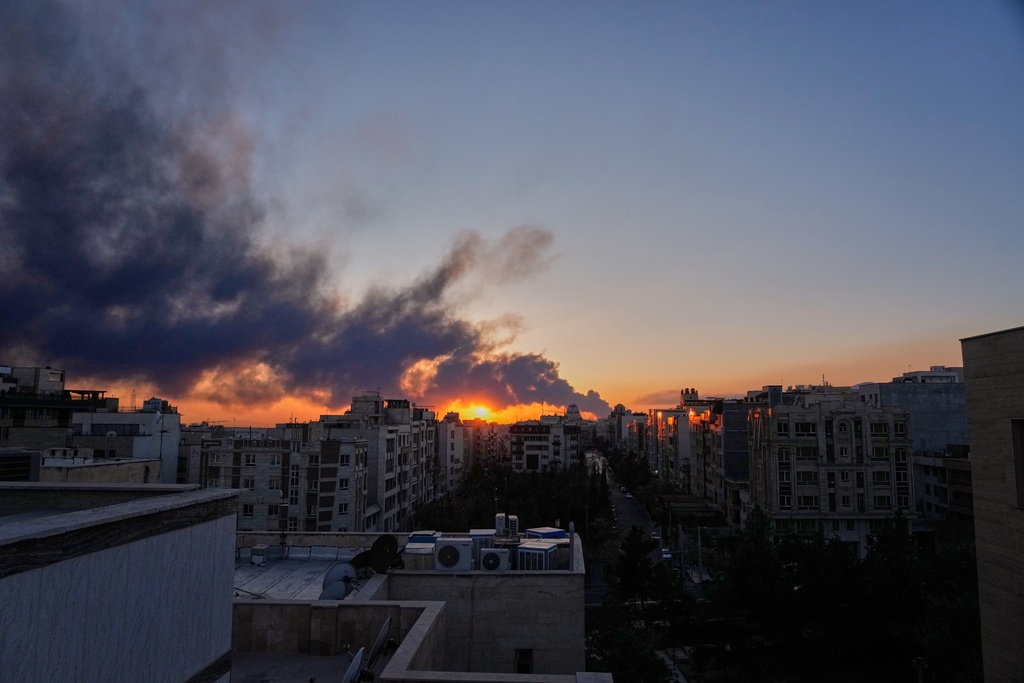 The sun sets behind a plume of smoke rising after a U.S.–Israeli military strike in Tehran, Iran, Tuesday, March 3, 2026. (AP Photo/Vahid Salemi)