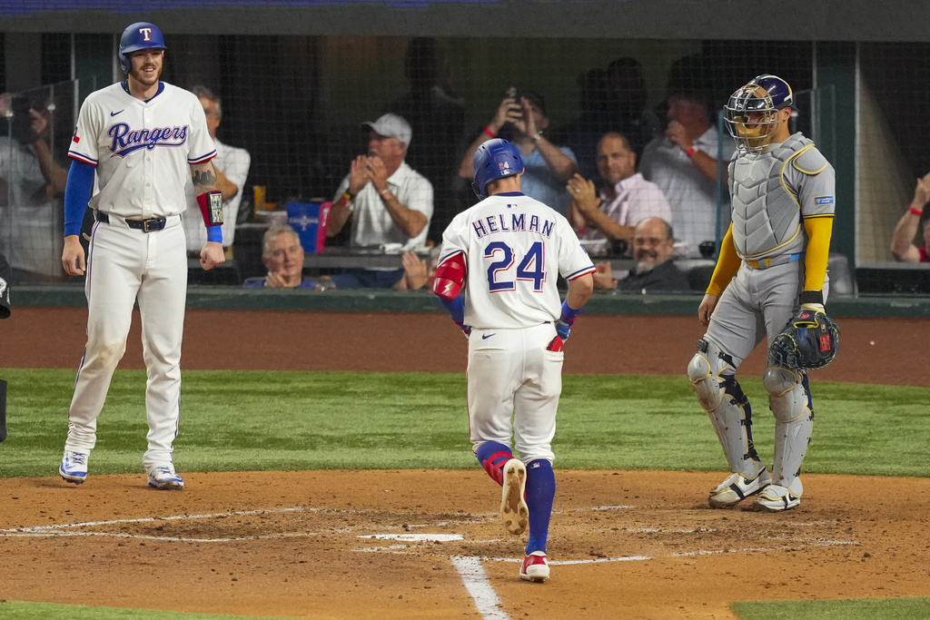 Texas Rangers' Michael Helman (24) prepares to cross home after hitting a two-run home run to score Jonah Heim, left, as Milwaukee Brewers catcher William Contreras, right, looks on during the fifth inning of a baseball game Tuesday, Sept. 9, 2025, in Arlington, Texas. (AP Photo/Julio Cortez)