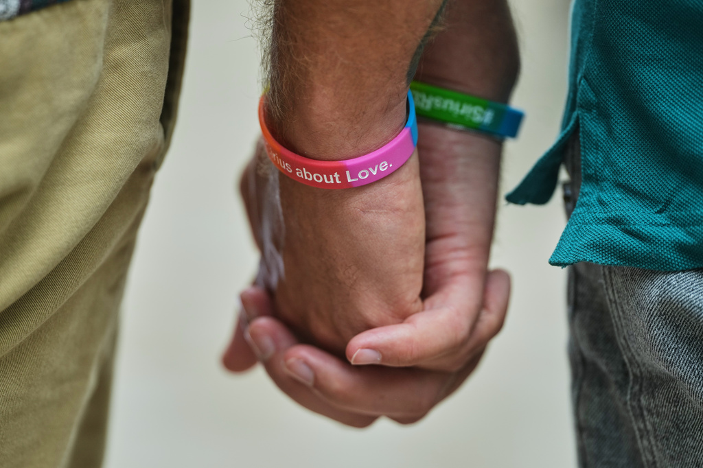 Two men hold hands at the memorial site commemorating the victims near the scene where a car rammed into a crowd near the Pride March in Berlin, Germany, Sunday, July 26, 2026. (AP Photo/Markus Schreiber)