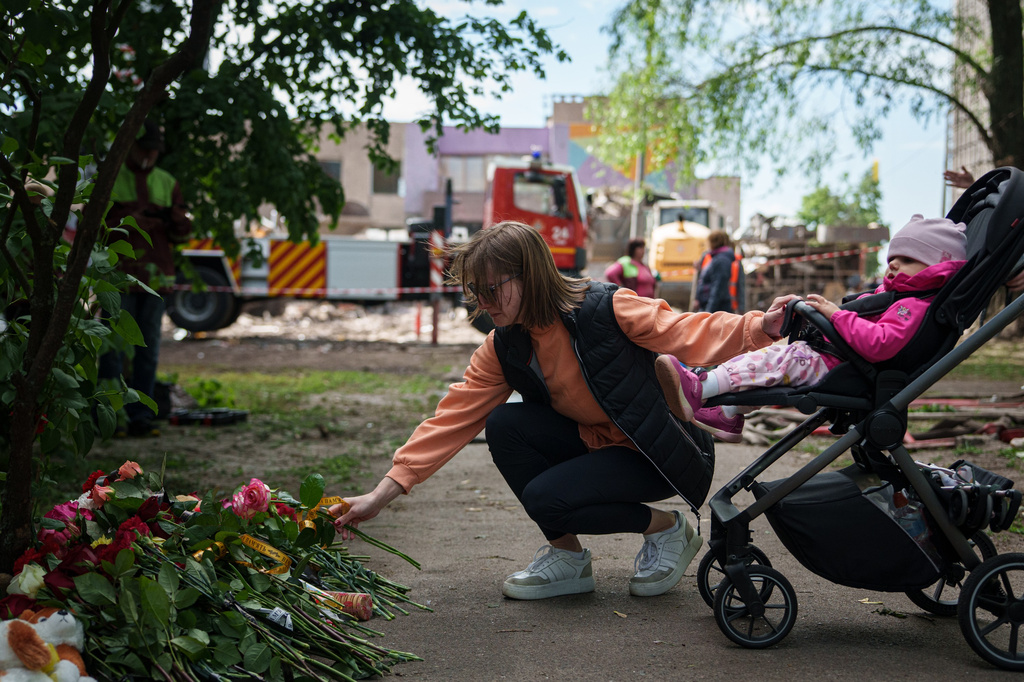 A woman lays flowers in front of a house heavily damaged after a Russian strike on residential neighbourhood in Kyiv, Ukraine, on Friday, May 15, 2026. (AP Photo/Evgeniy Maloletka)