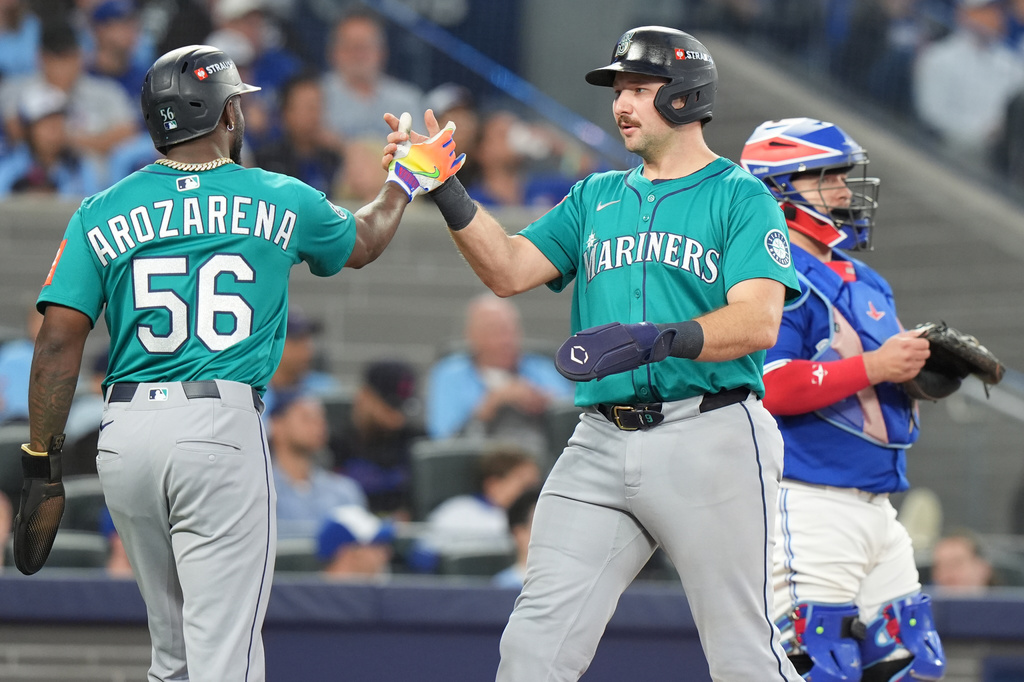 Seattle Mariners' Randy Arozarena (56) and Cal Raleigh, center, celebrate after scoring on a three-run home run by teammate Jorge Polanco during the fifth inning of Game 2 of baseball's American League Division Series against the Toronto Blue Jays in Toronto, Monday, Oct. 13, 2025. (Frank Gunn/The Canadian Press via AP)