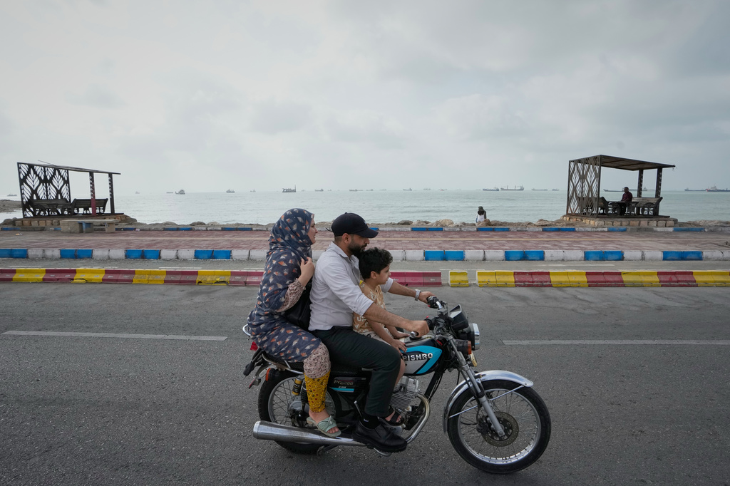 A man, woman and boy ride a motorcycle along the waterfront as commercial vessels lie anchored in the Strait of Hormuz off Bandar Abbas, Iran, Friday, Sept. 4, 2026. (AP Photo/Vahid Salemi)