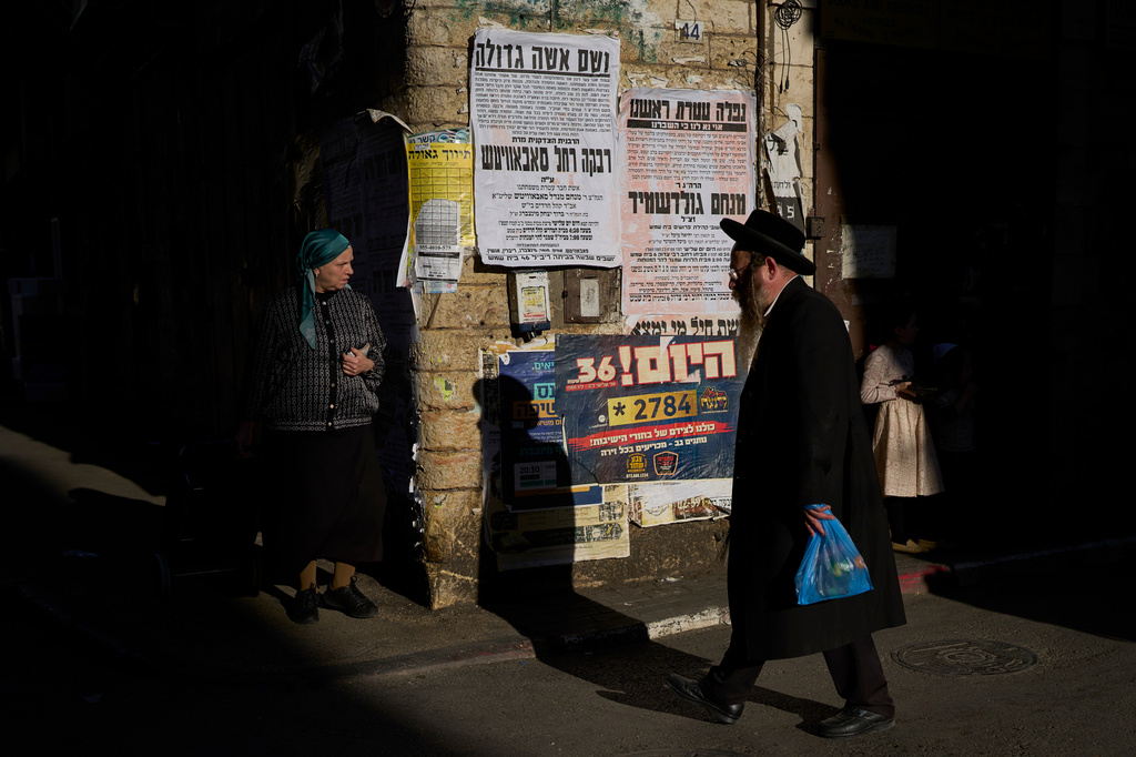 Ultra-Orthodox Jews walk past pashkevilim, posters used to publicize news and important messages in the ultra-Orthodox community, in the Mea Shearim neighborhood of Jerusalem, Wednesday, July 8, 2026. (AP Photo/Ohad Zwigenberg)