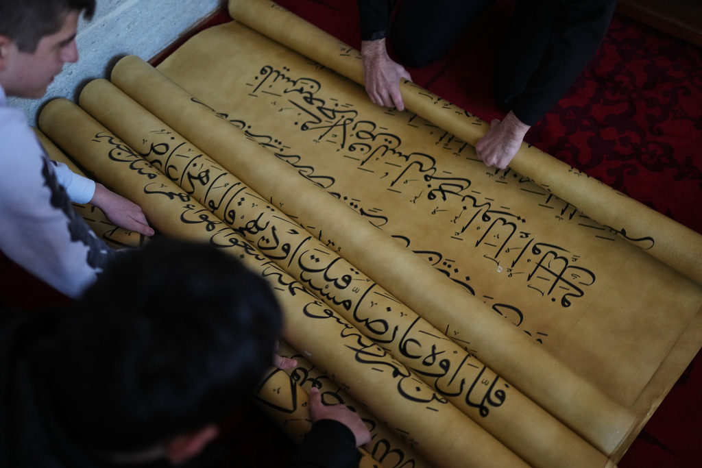 Islamic school students unroll scrolls of a massive handwritten manuscript of the Quran, Islam's holy book, by Iraqi calligrapher Ali Zaman, at the Mihrimah sultan mosque, in Istanbul, Turkey, Wednesday, Jan. 14, 2026. (AP Photo/Francisco Seco)