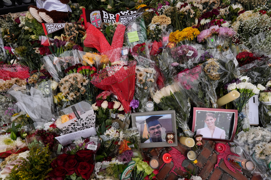 FILE - Photos of Brown University shooting victims Mukhammad Aziz Umurzokov, left, and Ella Cook, are seen amongst flowers at a makeshift memorial at the school's Van Wickle Gate, Dec. 17, 2025, in Providence, R.I. (AP Photo/Robert F. Bukaty, File)