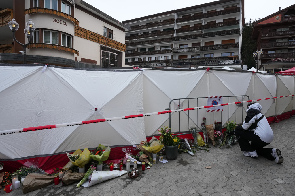 People bring flowers near the sealed off Le Constellation bar in Crans-Montana, Swiss Alps, Switzerland, Friday, Jan. 2, 2026, where a devastating fire left dead and injured during the New Year's celebrations. (AP Photo/ Antonio Calanni)